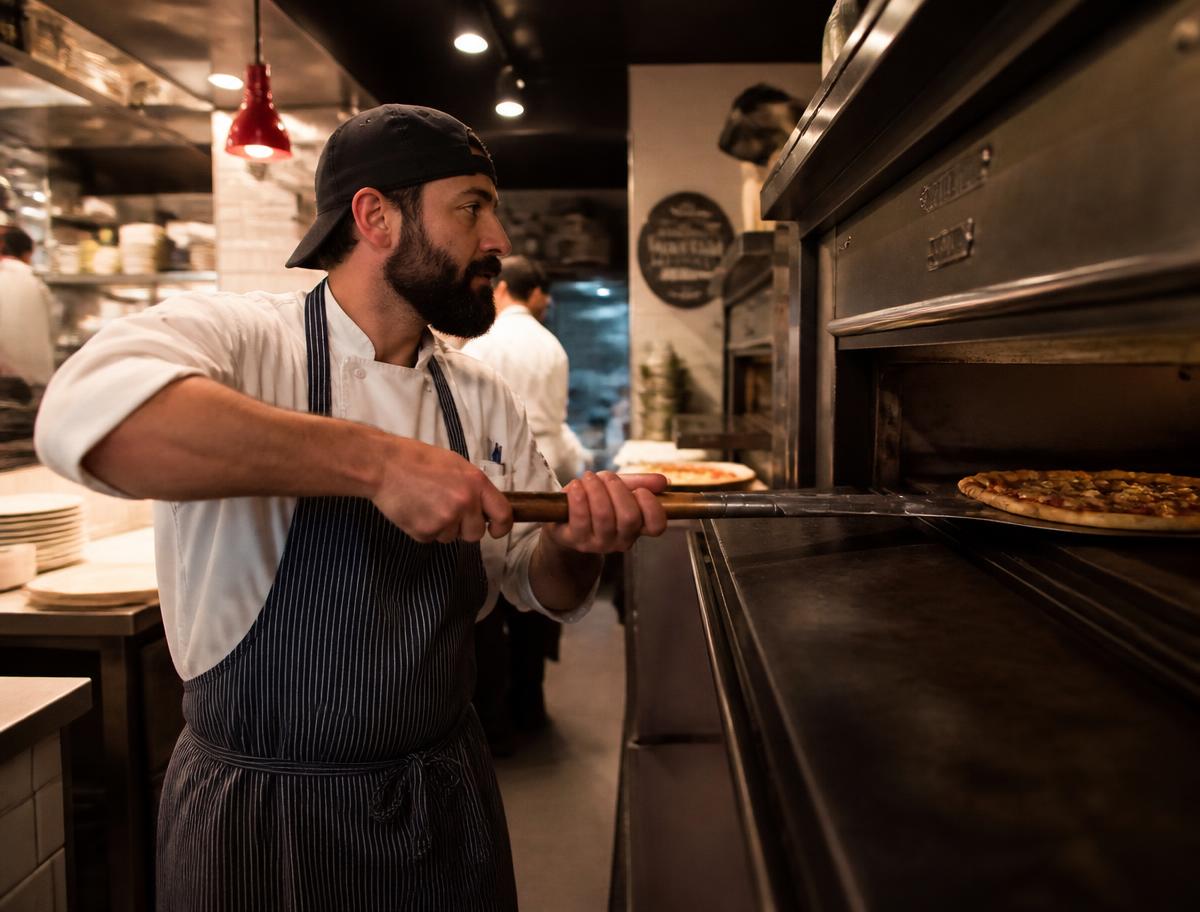 Chef sliding a pizza into the deck oven of a partner restaurant